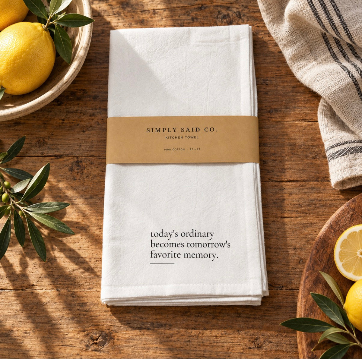 White cotton kitchen towel with quote displayed on rustic wood surface with lemons