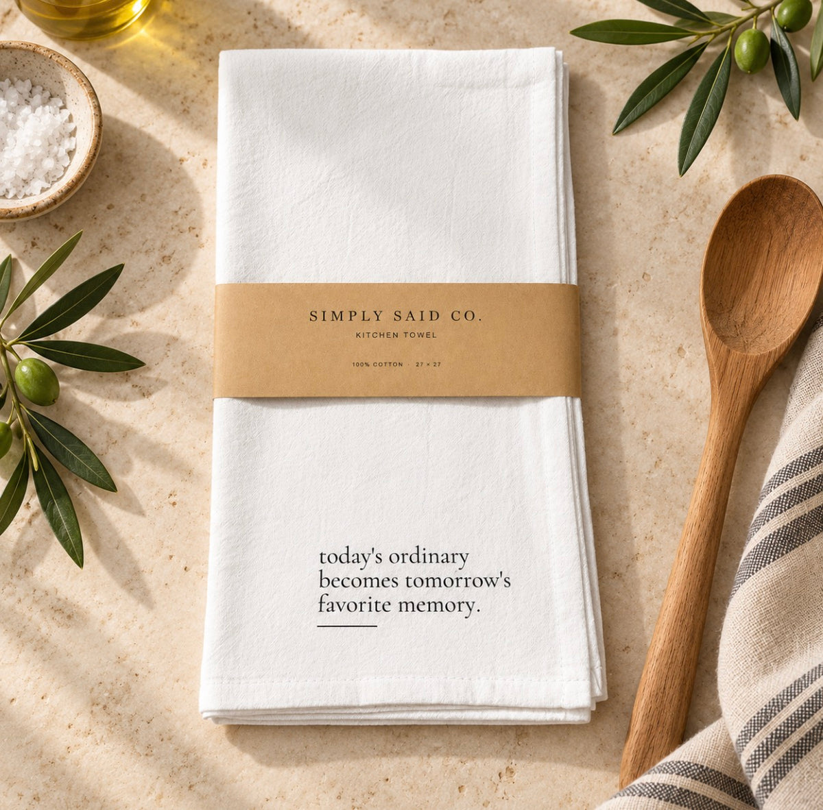 White cotton kitchen towel with quote and kraft belly band on a light stone background