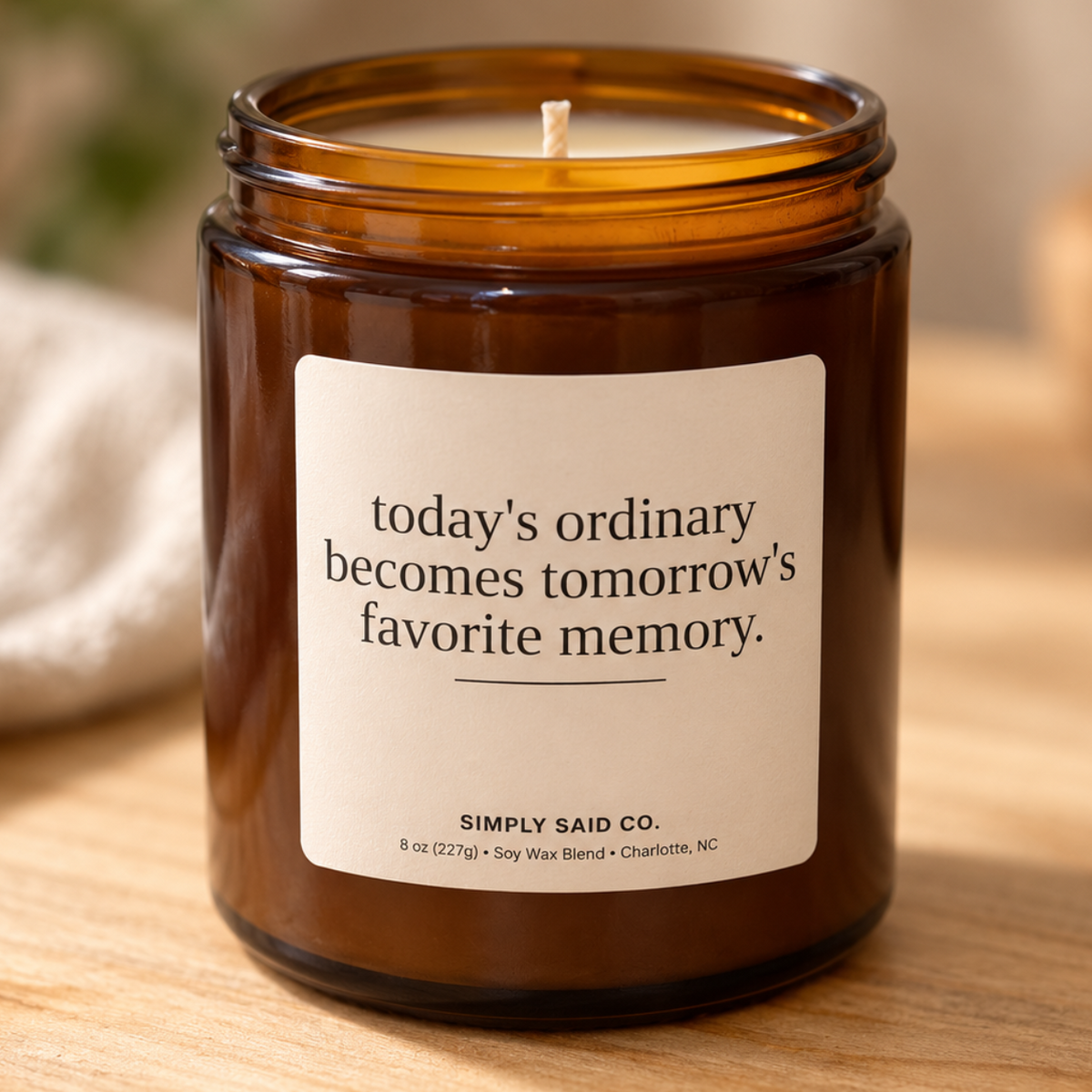 An amber glass jar candle with a white label that reads, 'today's ordinary becomes tomorrow's favorite memory.' by Simply Said Co.