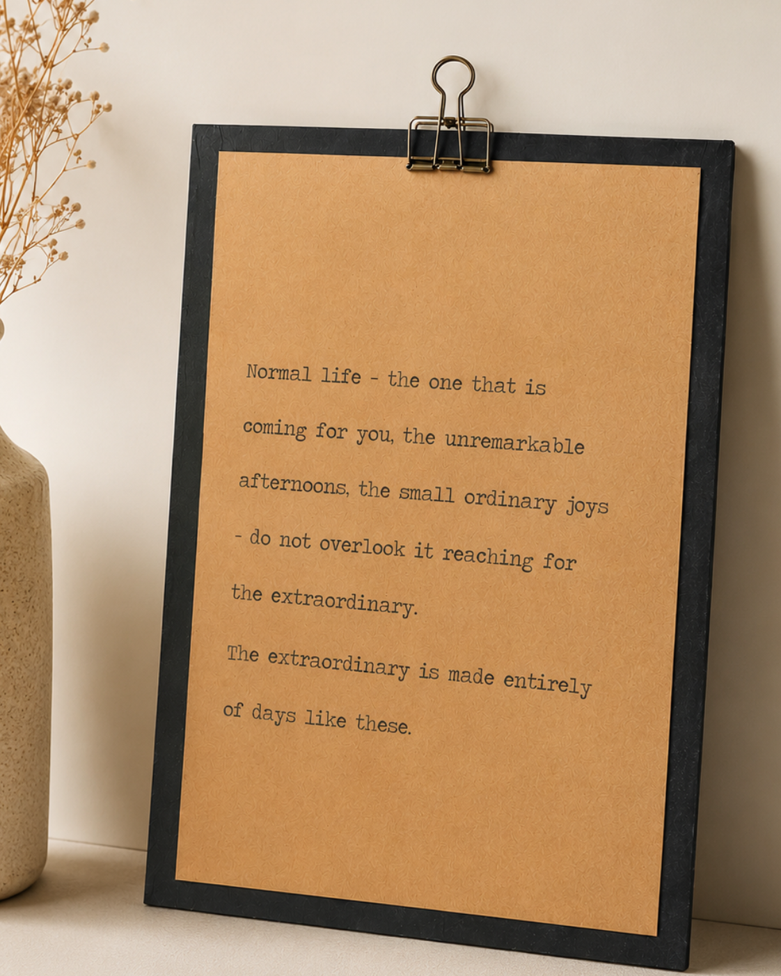 Minimal black and kraft wood sign featuring an inspirational quote about ordinary days displayed beside a neutral ceramic vase